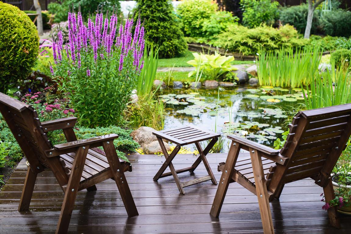 Garten neben der Terasse mit Tisch und zwei Klappstühlen mit den Blick auf einen Teich, Gartenzubehör bei topheim-plusgarten